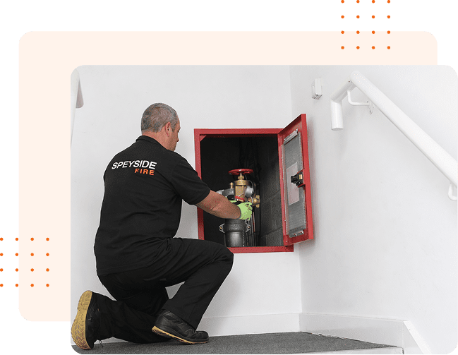 Technician inspecting a fire hose cabinet indoors.